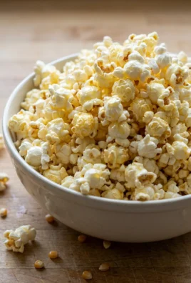 A white ceramic bowl filled with fluffy popcorn, drizzled with butter.