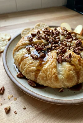A finished baked brie in puff pastry, drizzled with maple syrup and garnished with pecans.