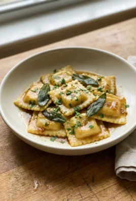 A plated bowl of lobster ravioli garnished with fresh parsley and sage leaves.