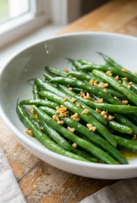 A white bowl filled with bright green sauteed green beans with garlic.